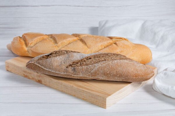 Barras de pan integral y pan de piña sobre tabla de madera, representando la variedad en una panadería.