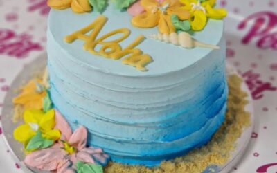 Tarta de cumpleaños personalizada decorada en azul con flores y mensaje "Aloha", ideal para celebraciones temáticas.