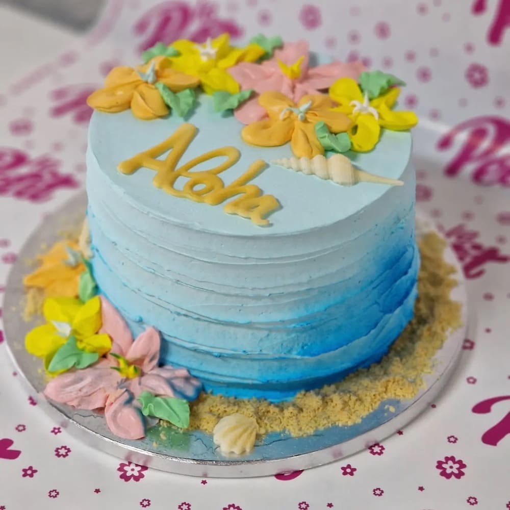 Tarta de cumpleaños personalizada decorada en azul con flores y mensaje "Aloha", ideal para celebraciones temáticas.